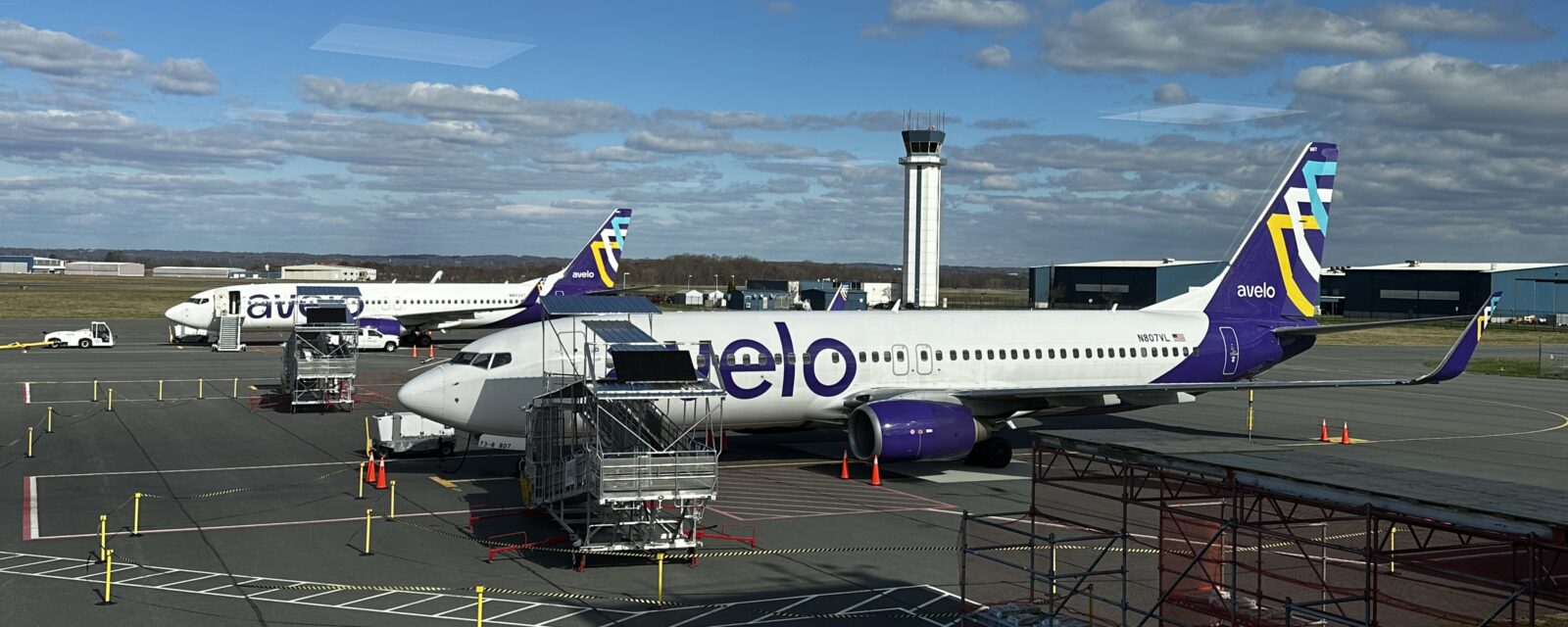Avelo airplanes parked on a runway with a control tower and clear blue sky.