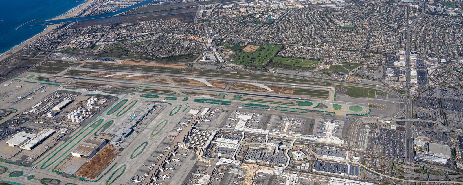 Aerial view of LAX airport, runways, terminals, and surrounding cityscape near the coast.