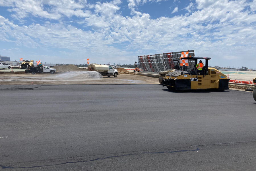 Construction vehicles and workers on airport taxiway under clear sky.
