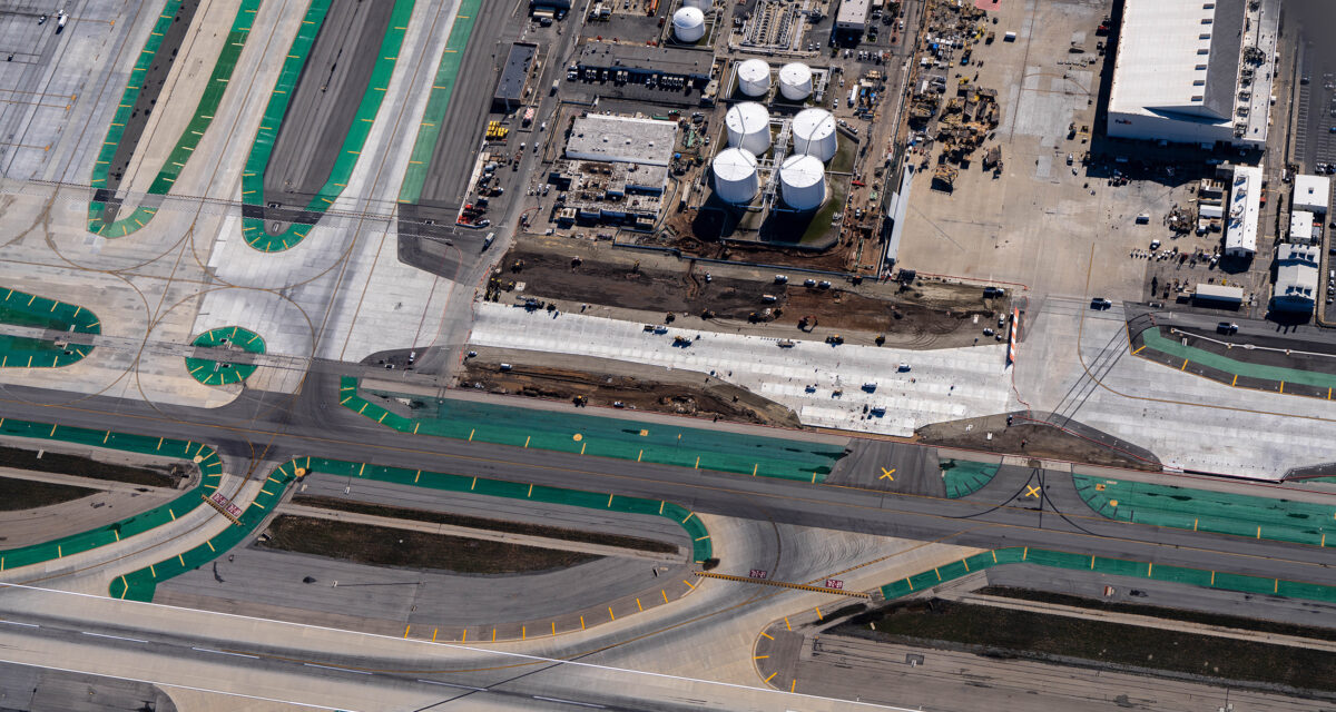 Aerial view of airport taxiways and construction site near fuel storage tanks.