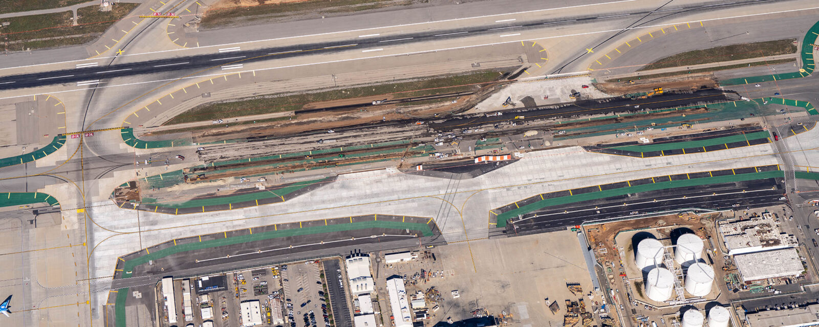 Aerial view of taxiway intersection under construction at an airport, with visible machinery and adjacent runways.