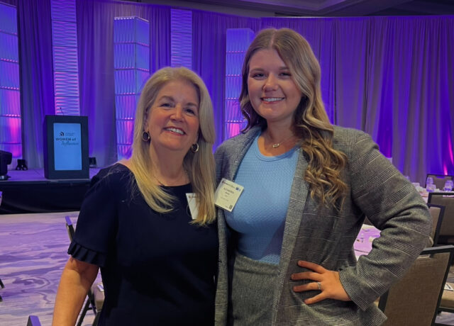 Two women smiling at an event, with purple-lit curtains in the background.