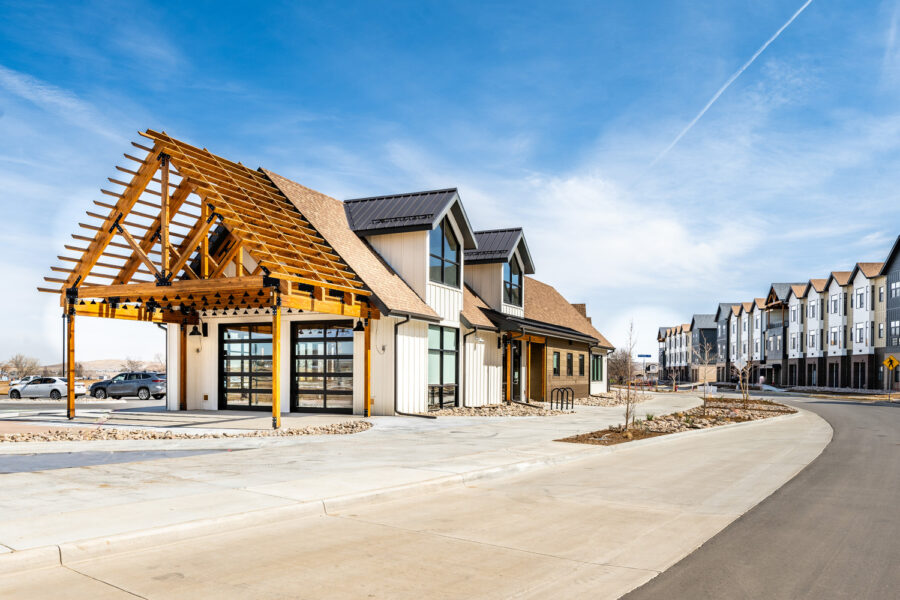 Modern residential building with exposed wooden framework and adjacent townhouses under a clear blue sky