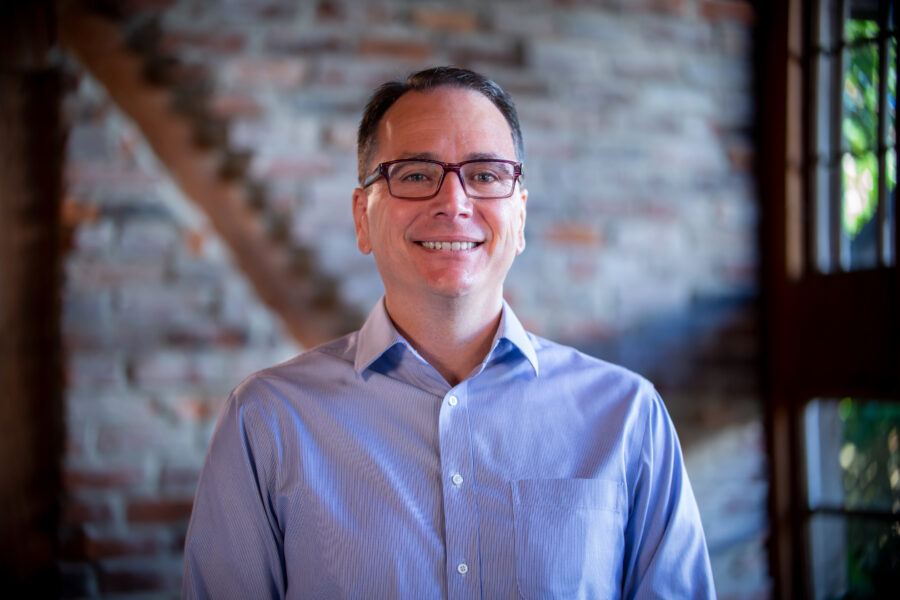 Steve Creamer smiling in front of a brick wall background