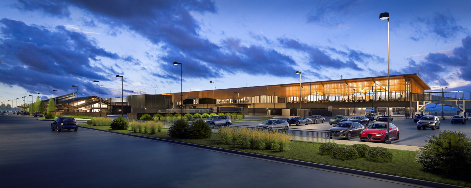 Night view of modern airport terminal, cars parked, under a cloudy sky.